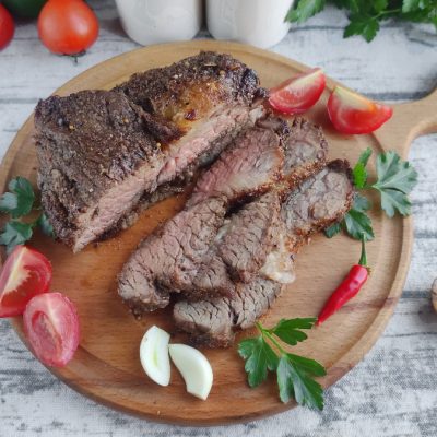 Air fryer steak on a wooden cutting board with tomatoes and herbs.