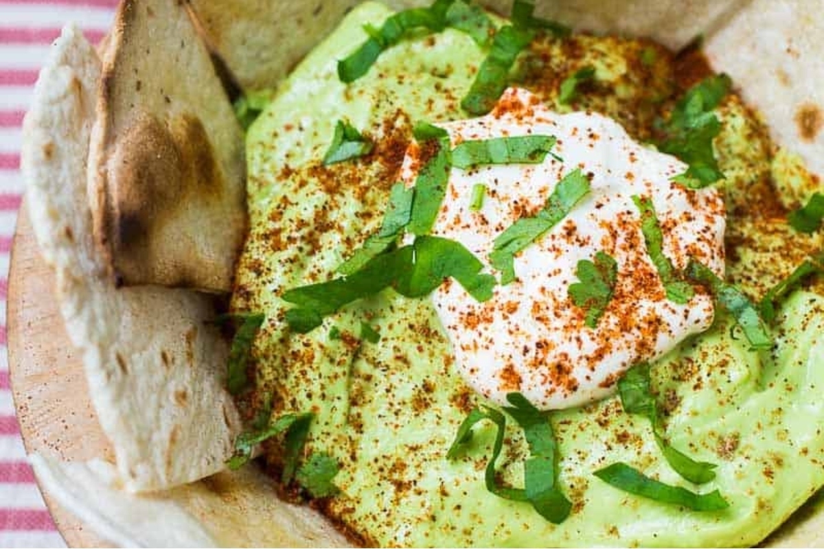 A bowl of hummus with pita bread and sour cream dips.