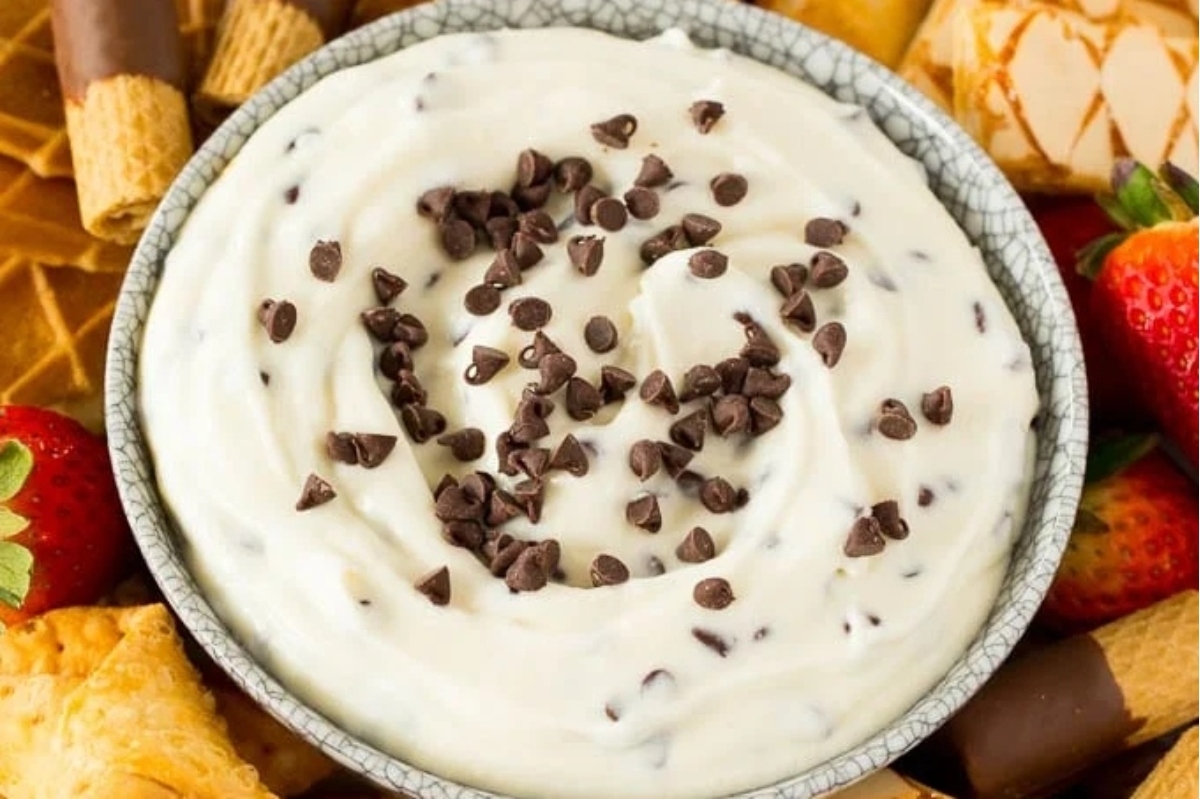 A bowl of chocolate chip cookie dough dip surrounded by strawberries, crackers, and cream cheese.