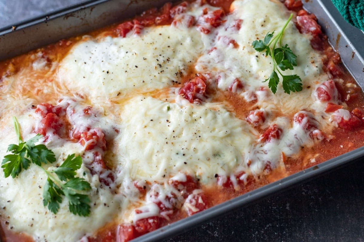 A cheesy casserole dish with tomatoes and parsley.