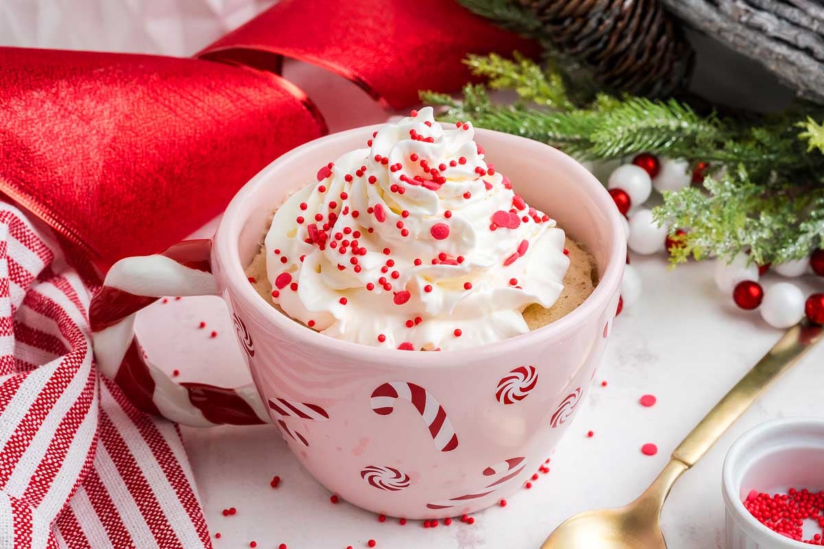 A steaming mug of hot cocoa topped with fluffy whipped cream and garnished with a festive candy cane.