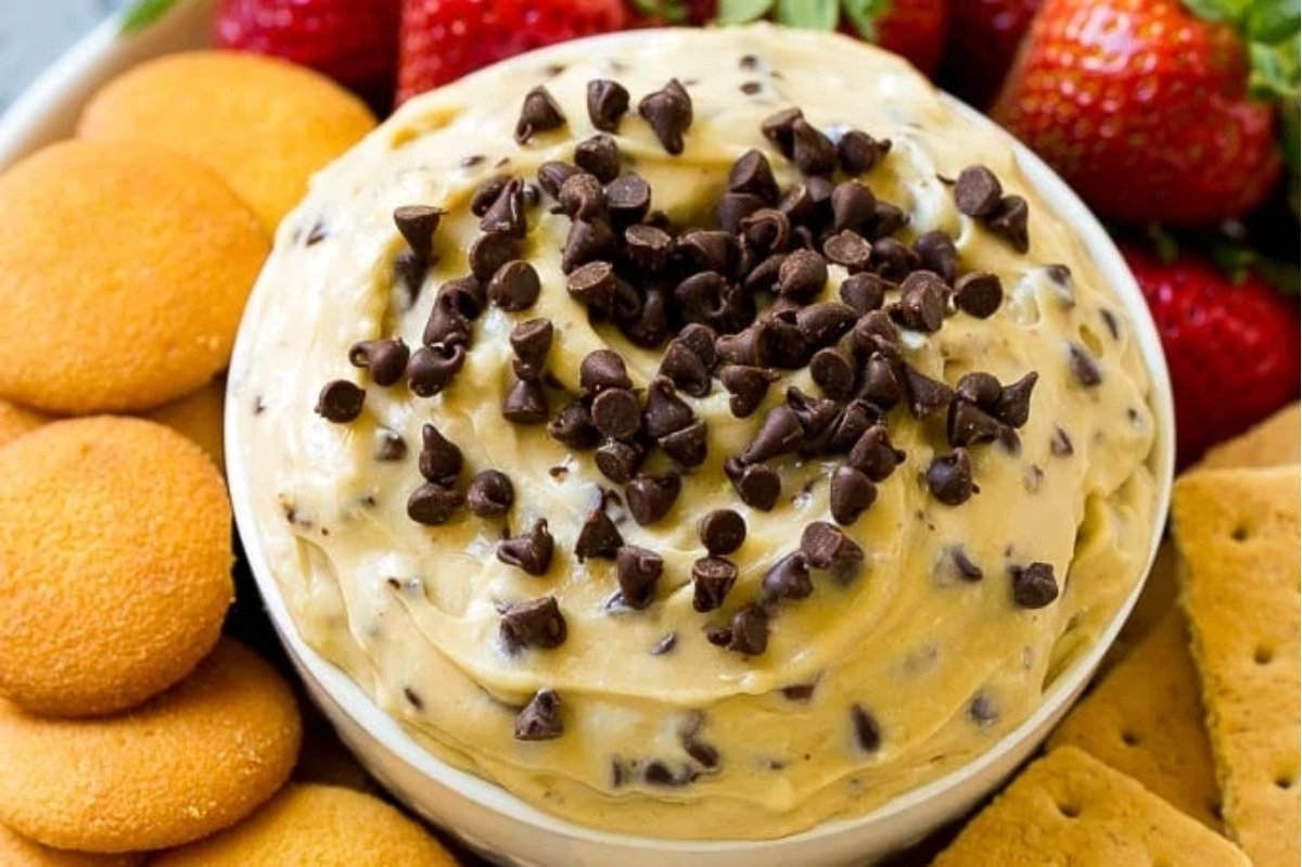 A creamy bowl of chocolate chip cookie dough dip served with strawberries and crackers.