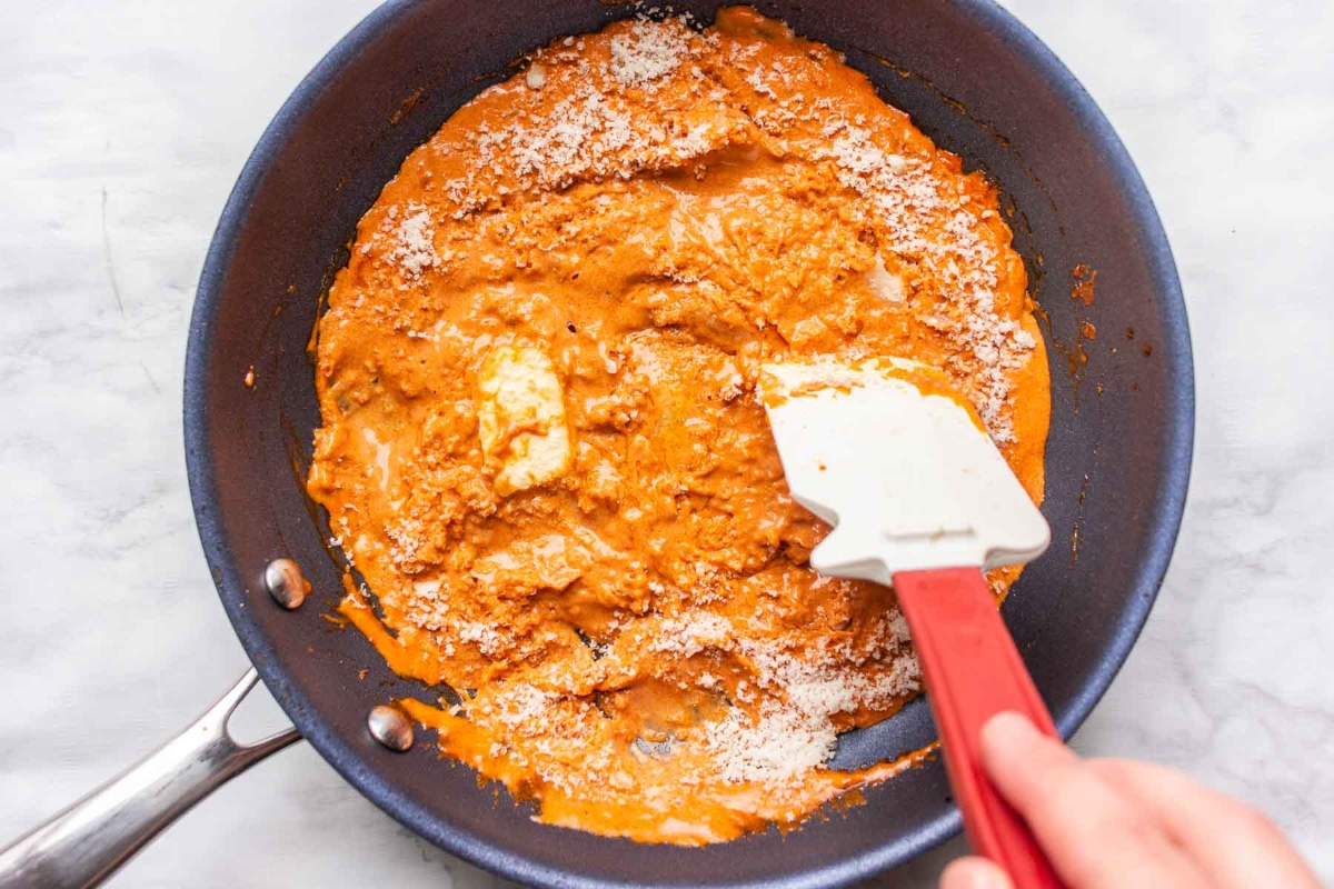 Gigi Hadid using a red spatula to stir pasta sauce in a pan.