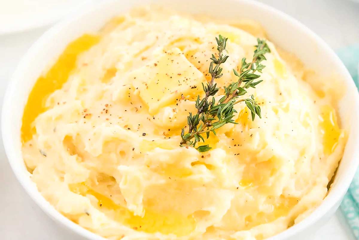 A bowl of Mashed Potatoes with a sprig of thyme.