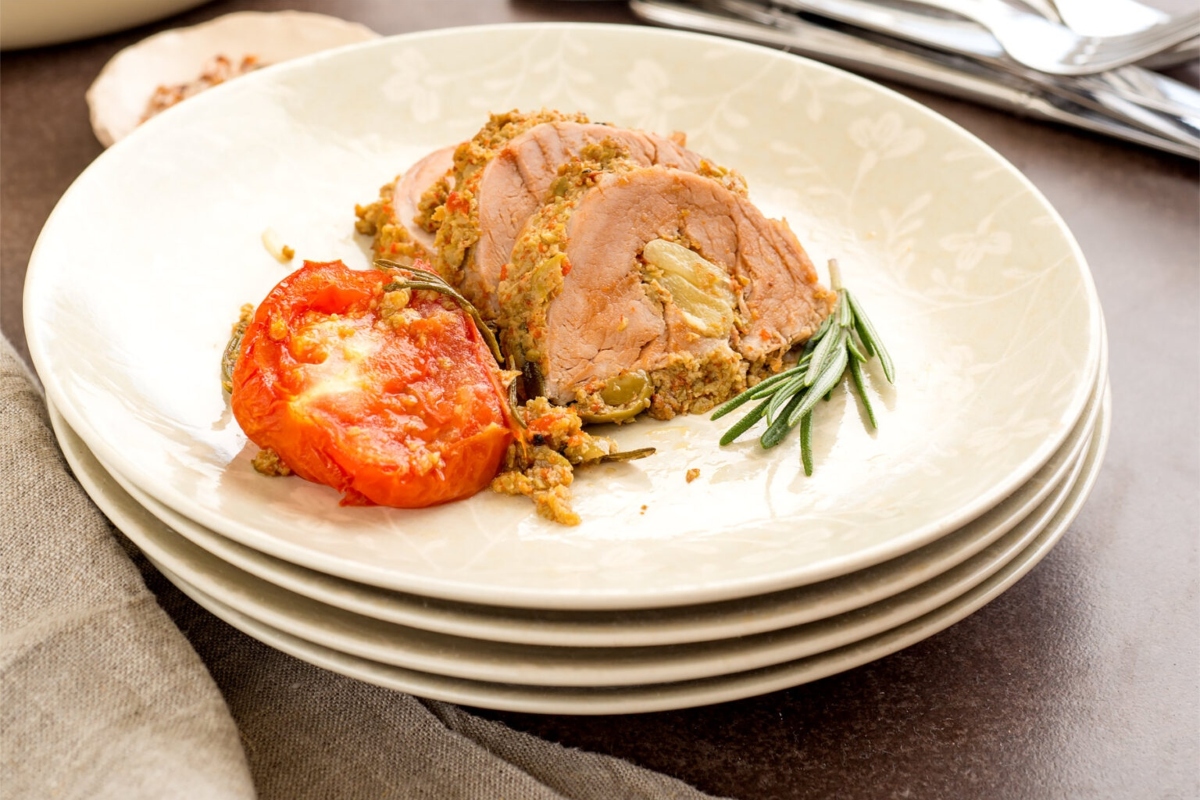 A plate with pork and tomatoes on it.