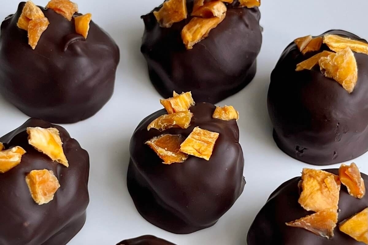 A group of chocolate covered oranges on a white plate.