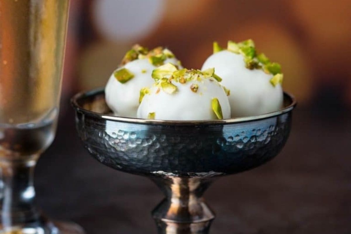 Pistachio truffles in a silver bowl next to a glass of champagne.