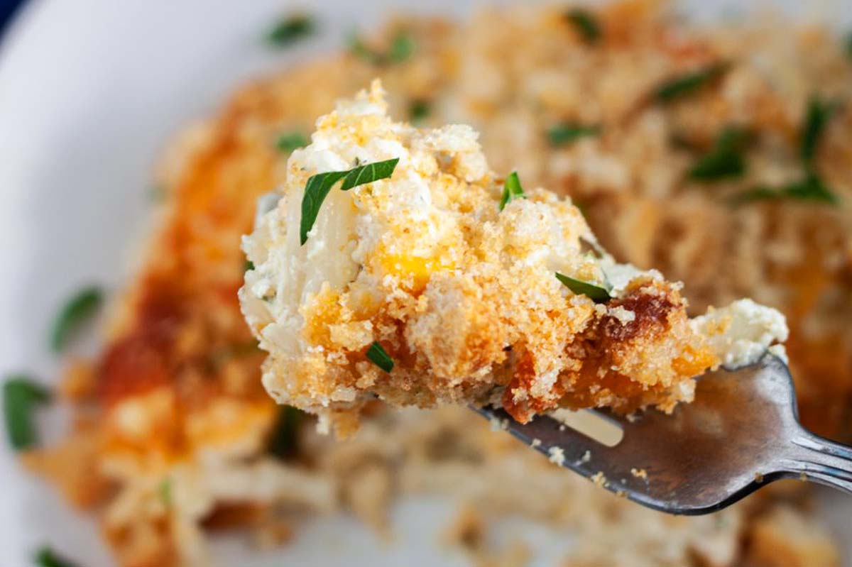 A country-style fork is holding a piece of cheesy casserole, perfect for holiday recipes.