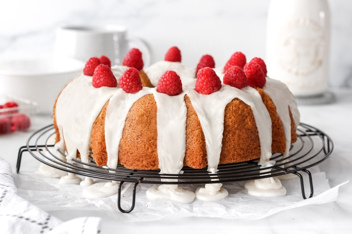 A Valentine's Day bundt cake with icing and raspberries on a cooling rack.
