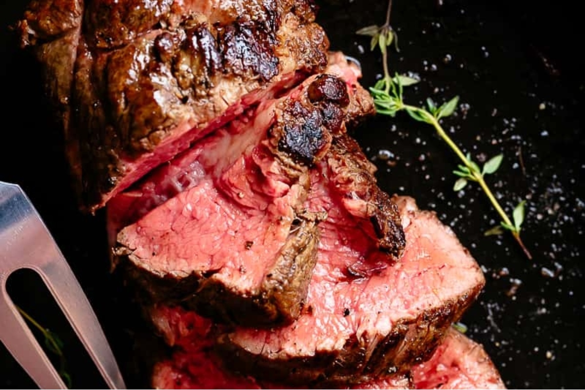 A succulent piece of beef steak sizzling on a black pan, ready to be enjoyed with a fork during Christmas dinner.