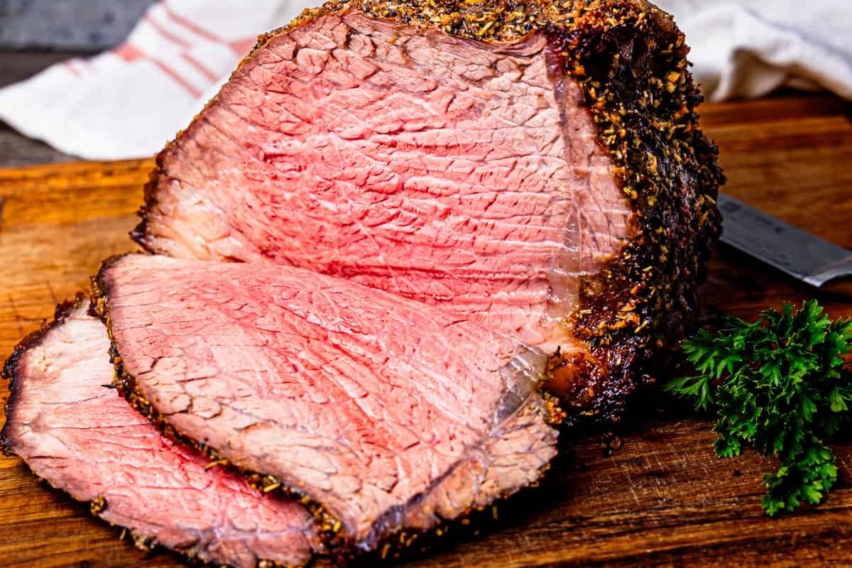 A sliced beef roast on a wooden cutting board.