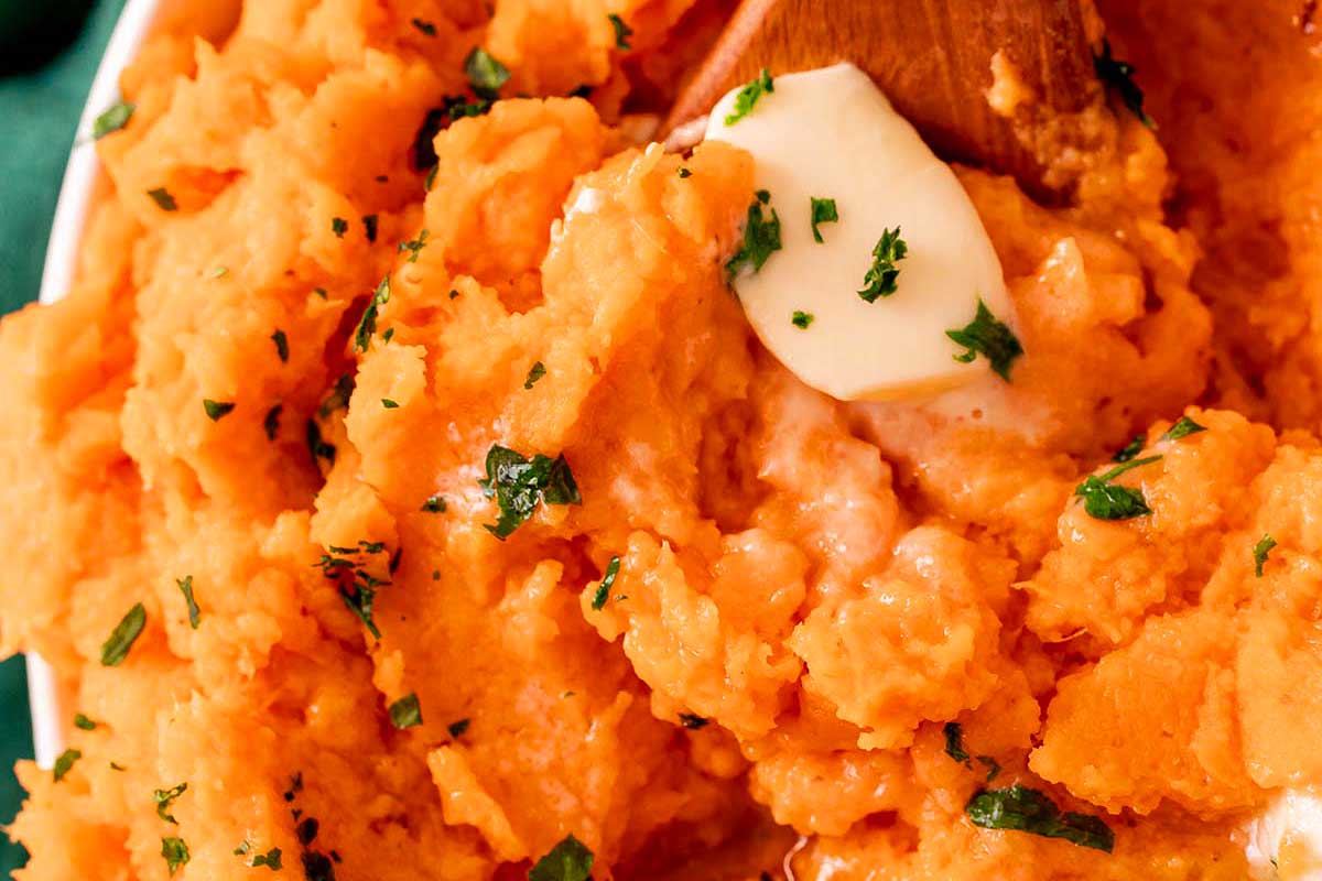 A bowl of Mashed Potatoes with butter and parsley.