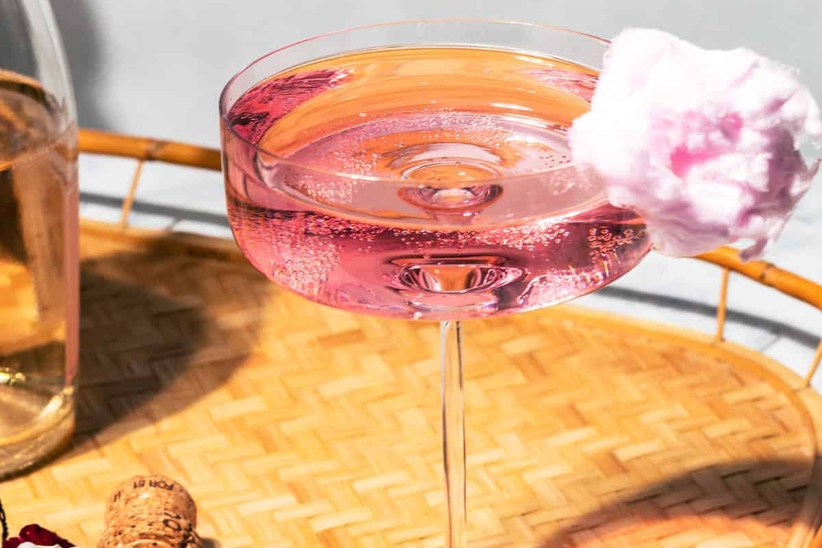 A pink cocktail, perfect for Valentine's Day, is sitting on a tray next to a bottle of wine.