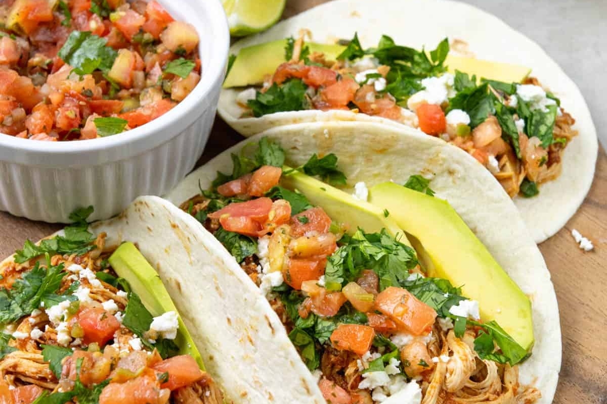 Three chicken tacos on a wooden cutting board.