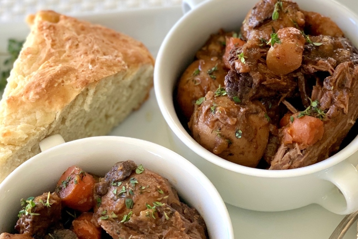 Two bowls of beef stew with carrots and bread.
