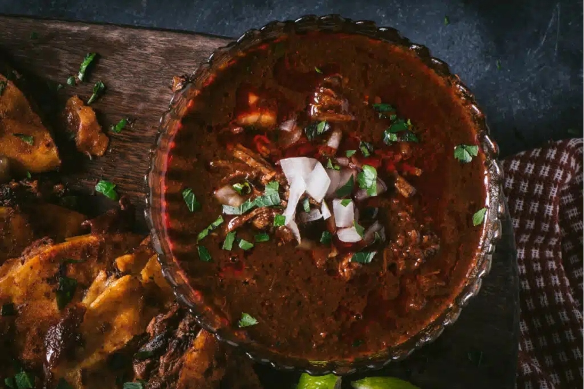 A bowl of chili and tortilla chips on a wooden table.