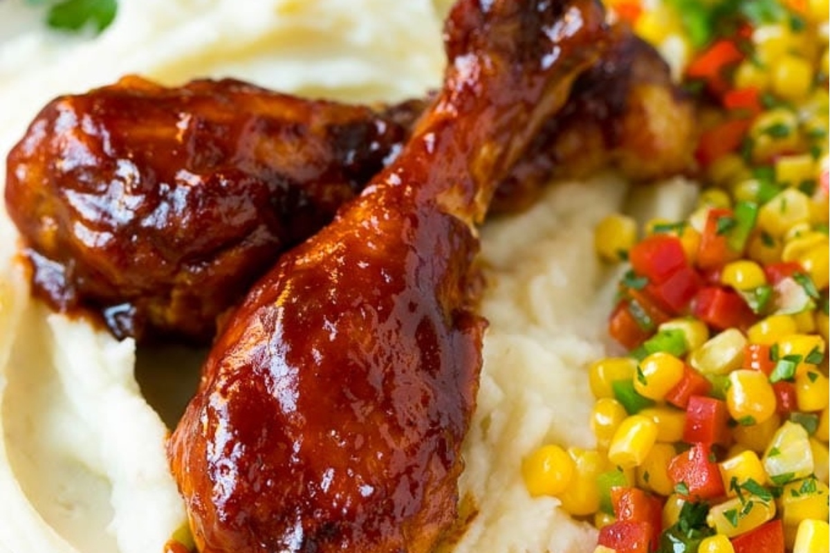 Bbq chicken legs on a plate with mashed potatoes and corn.