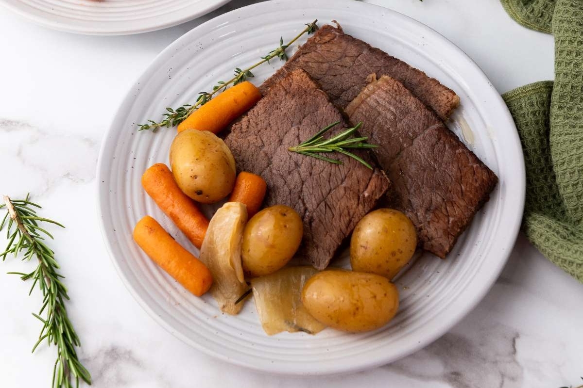 A plate with roast beef, carrots, potatoes and rosemary.