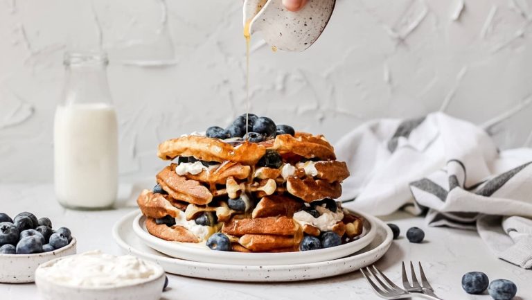A stack of blueberry pancakes with whipped cream and blueberries.