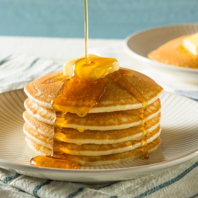 A stack of pancakes is being drizzled with syrup and suggestions on how to reheat pancakes.