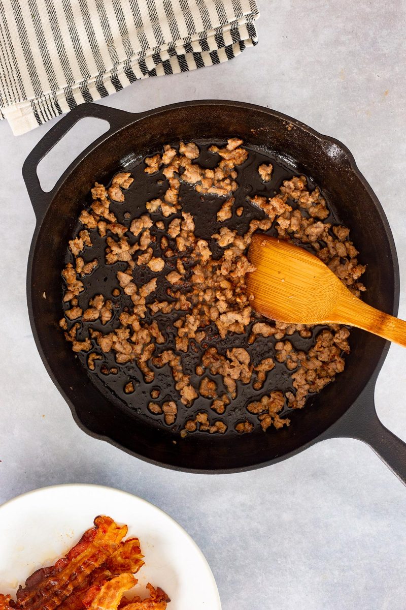 Loaded mac and cheese with bacon cooked in a skillet using a wooden spoon.