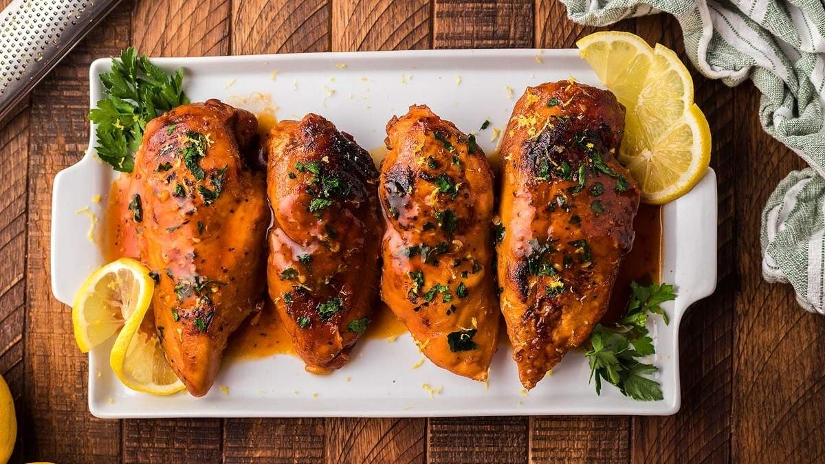 Grilled chicken breasts served on a white plate with lemon wedges - a delightful comfort food recipe.