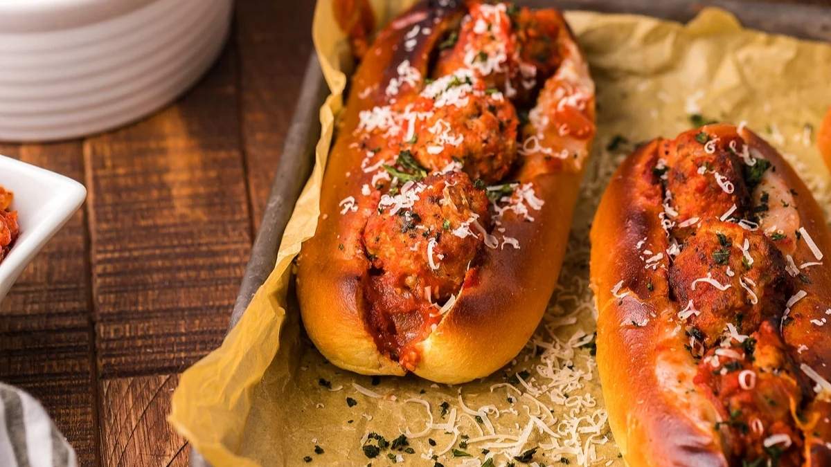 Two shared hot dogs on a baking sheet with sauce and parmesan.