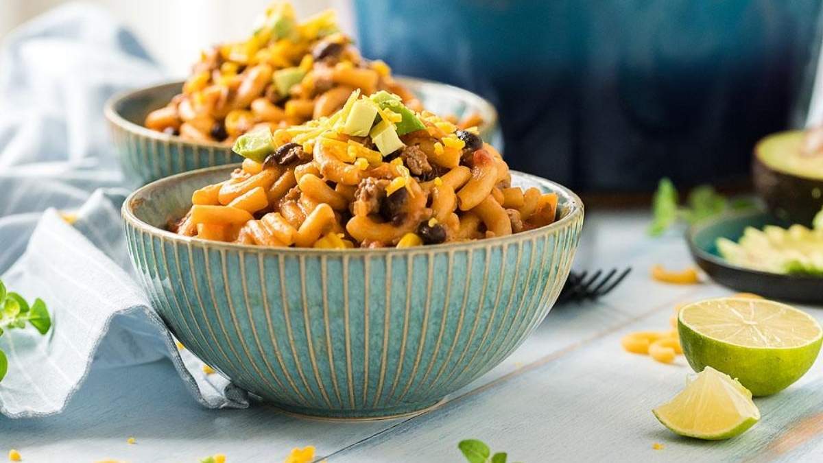 Two bowls of comfort food pasta, shared and served with avocado and lime on a table.