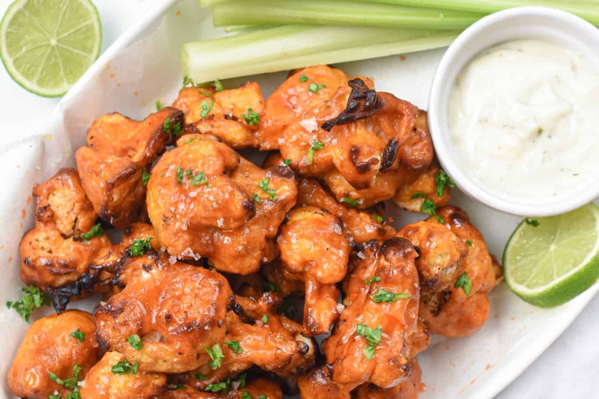 Buffalo chicken wings on a white plate with limes and celery.