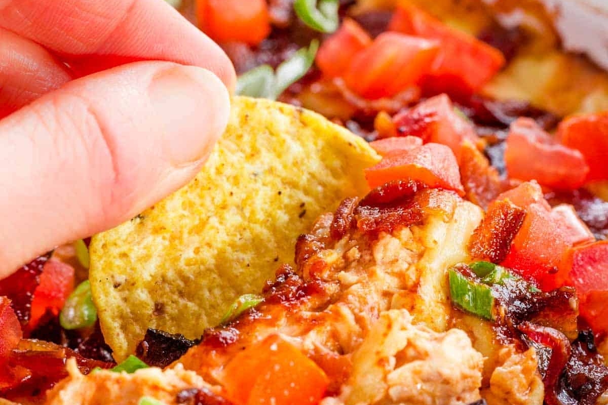 A person is dipping a tortilla into a bowl of dip.
