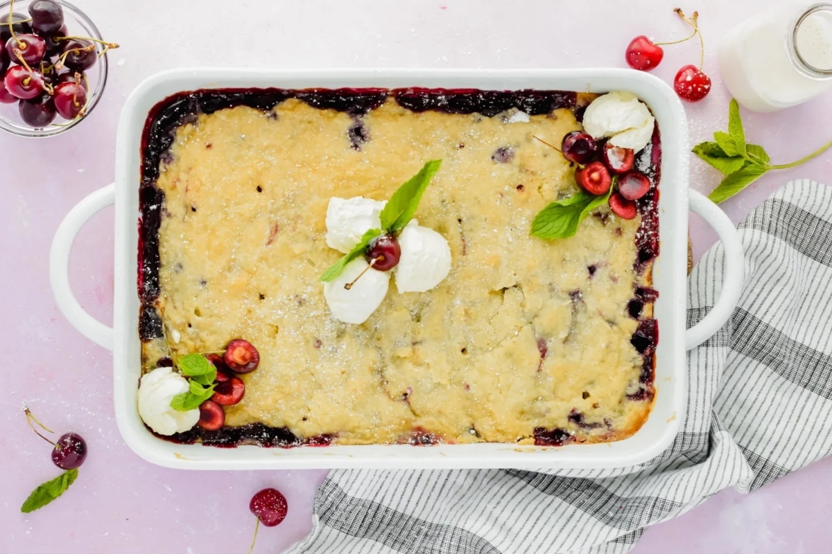 Cherry cobbler in a white dish with whipped cream and cherries.