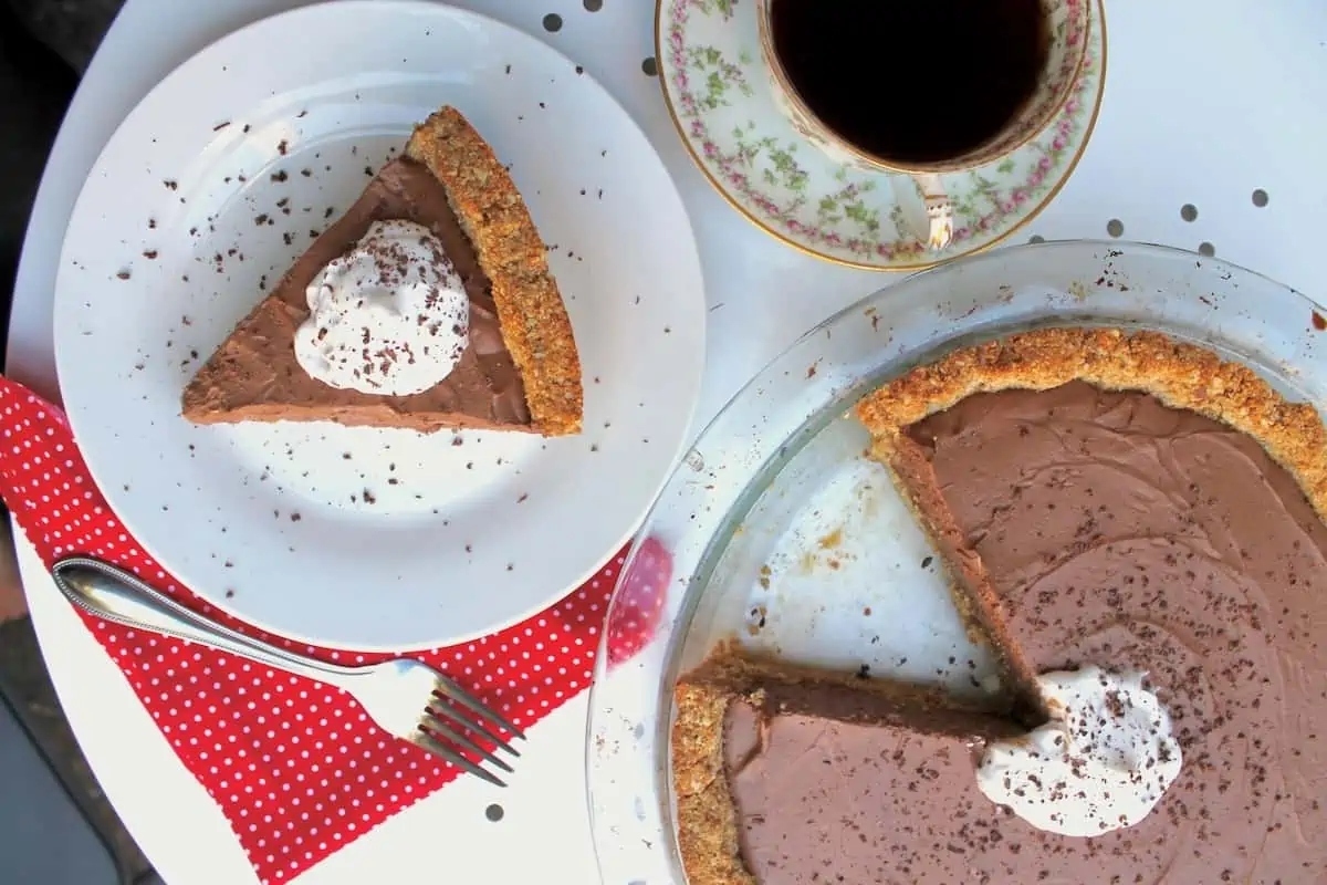 A slice of chocolate pie on a plate with a cup of coffee.