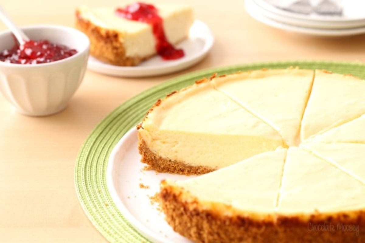 A slice of cheesecake on a plate next to a cup of jam.