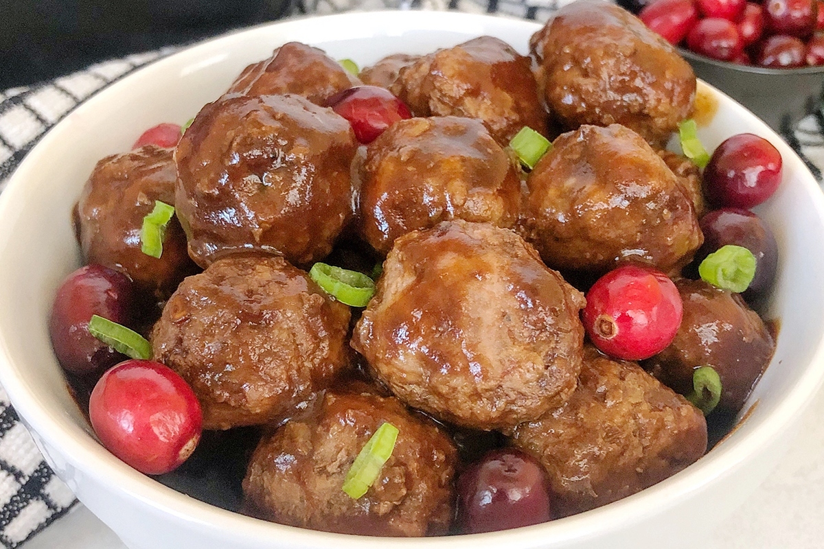 Cranberry meatballs in a white bowl with cranberries.