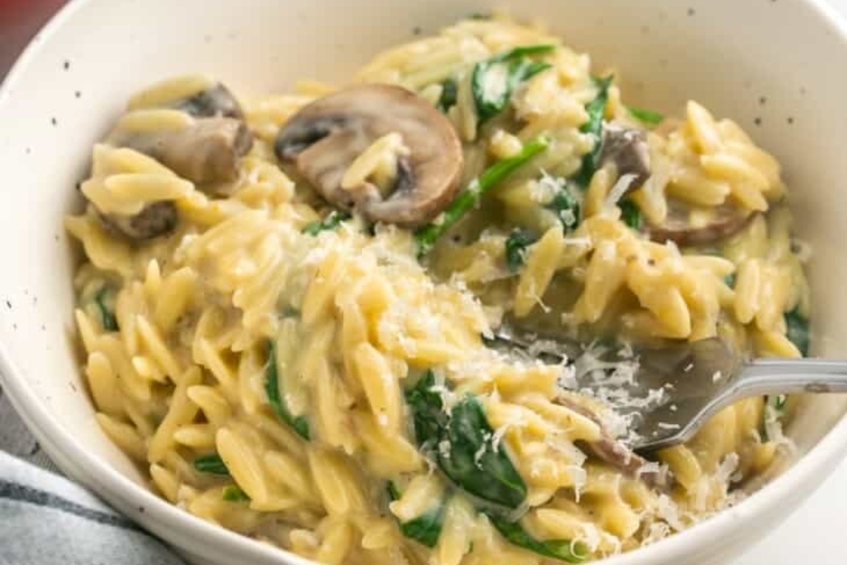 A bowl of pasta with mushrooms and spinach.