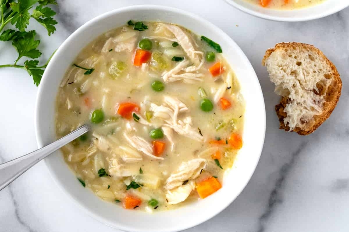 A bowl of chicken noodle soup with bread and carrots.