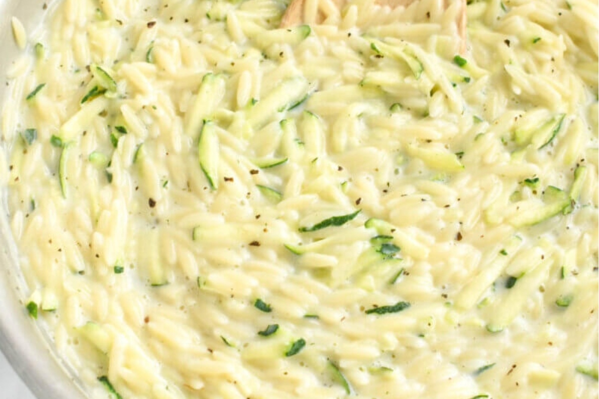 Zucchini risotto in a pan with a wooden spoon.