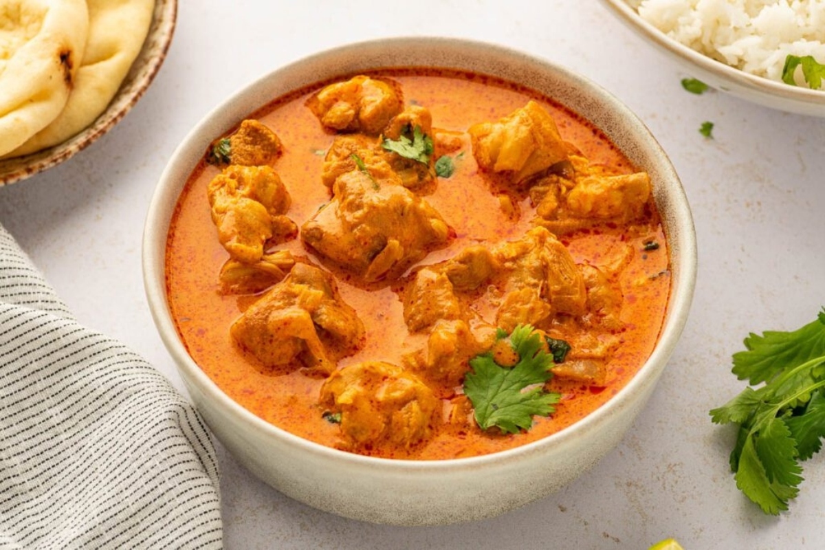A bowl of chicken curry with rice and bread.