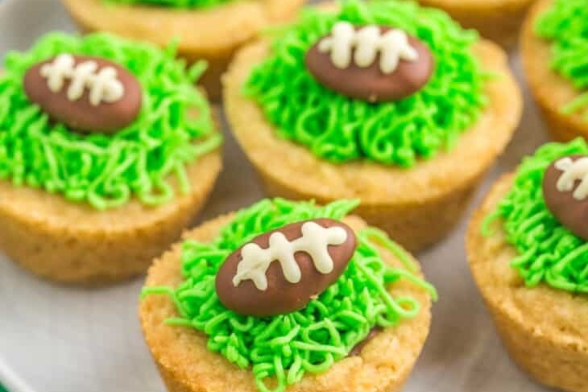 Football cupcakes with green frosting on a plate.
