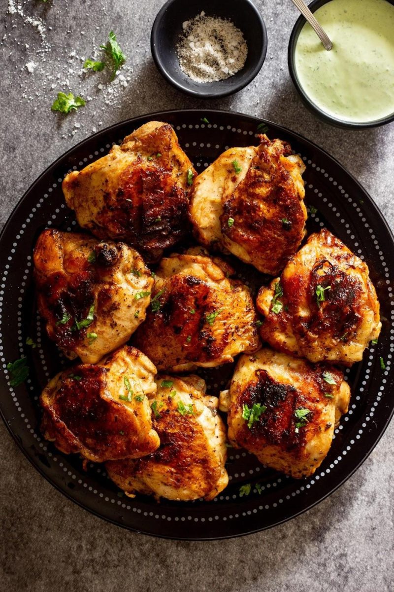 Grilled chicken thighs on a black plate.