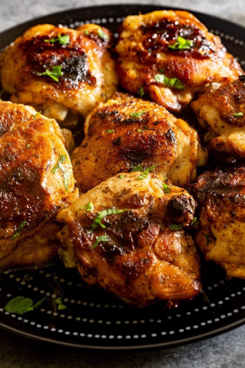 Grilled chicken thighs on a black plate.
