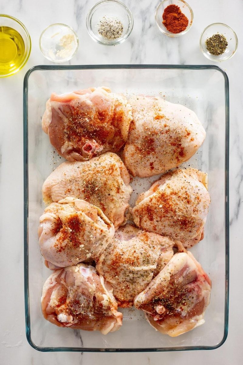 Raw chicken thighs marinating in a glass baking dish.