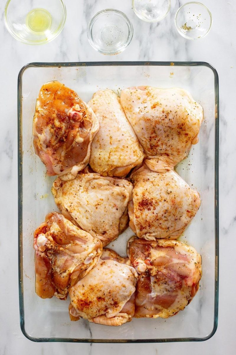 Raw chicken thighs marinating in a glass baking dish.