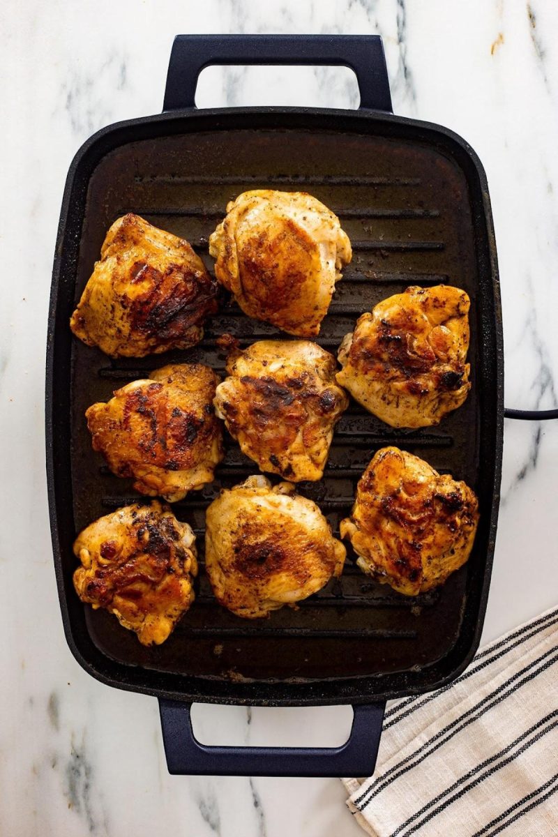 Grilled chicken thighs in a pan on a marble countertop.