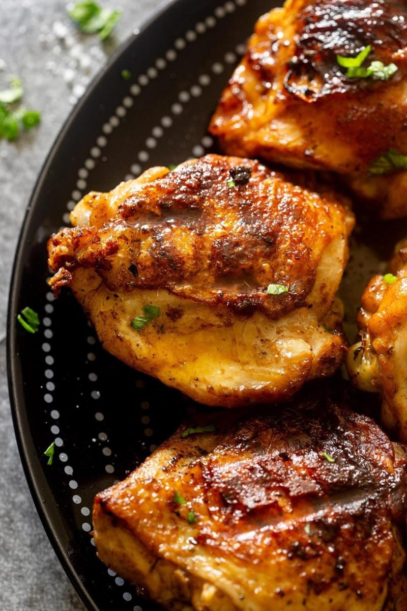 Grilled chicken thighs on a black plate.