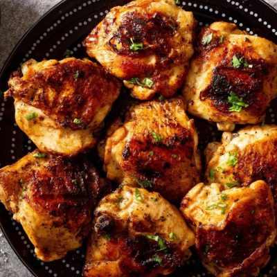 Grilled chicken thighs on a black plate.