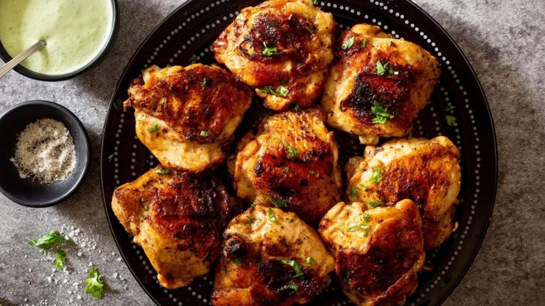 Grilled chicken thighs on a black plate.