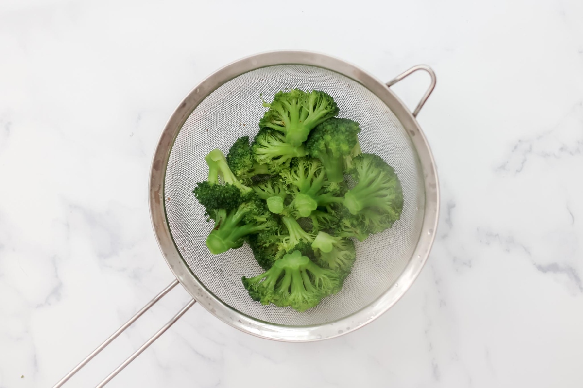 Broccoli in a strainer on a marble countertop.
