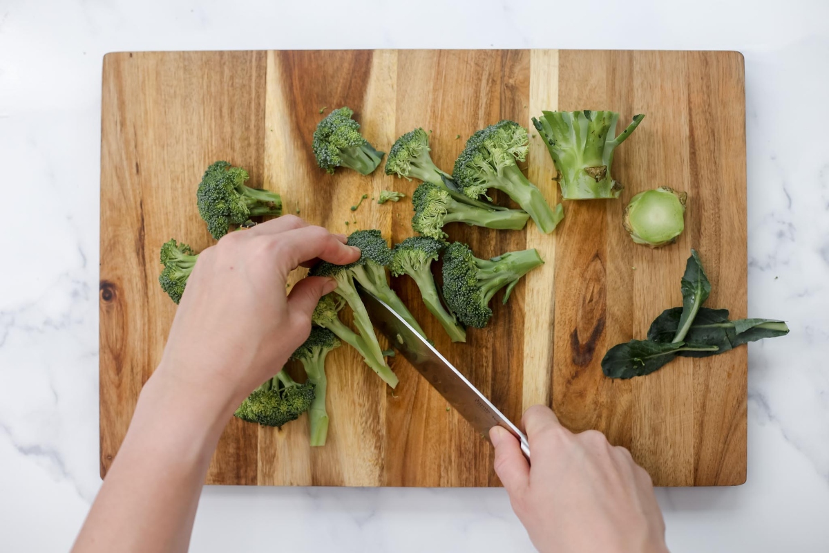 A person chopping broccoli on a cutting board.