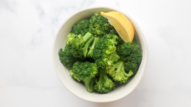 A bowl of broccoli with a slice of lemon.
